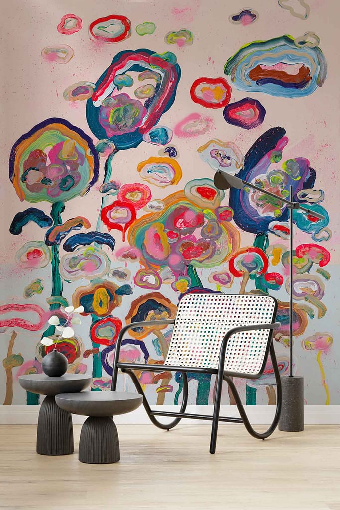 A vibrant abstract floral mural dominates the background. The wallpaper features bold splashes of red, pink, and orange interspersed with deep green leaves on a white base. Florals blend seamlessly into an array of dynamic brushstrokes and color gradients, creating a lively yet sophisticated backdrop. Keywords: vibrant abstract floral mural, red flowers, pink blossoms, orange accents, green leaves, white background.