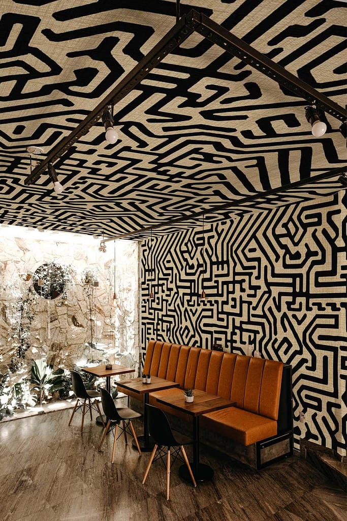 The cafe features abstract black and white maze-like patterns covering the wallpaper on the walls and ceiling. The design is intricate, with a monochrome palette that creates a striking visual effect.