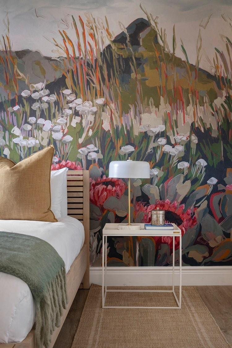 The wallpaper features a vibrant floral mural showcasing an array of colors, including bold reds, soft pinks, sunny yellows, lush greens, and deep blues. Floral patterns include whimsical roses, playful daisies, and elegant peonies intertwined with leafy vines. This artistic wallpaper serves as a stunning focal point in the bedroom's design.