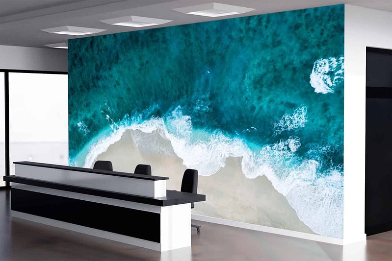 The wallpaper showcases a stunning beach scene featuring turquoise waves crashing onto the shore. The vibrant blue and green hues of the water contrast beautifully with the sandy shoreline, creating a serene coastal vibe. Touches of white in the foamy waves add dynamic movement to this tranquil mural.