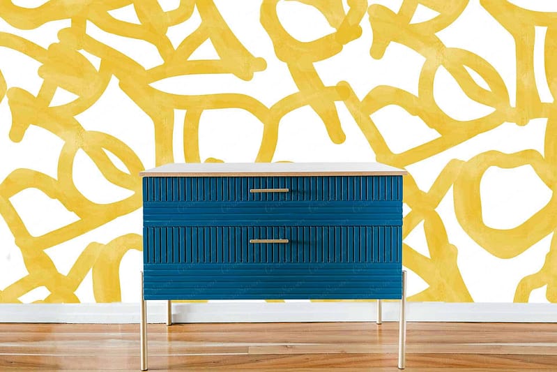 Abstract yellow pattern, white wall, bold design, tangled shapes or letters.