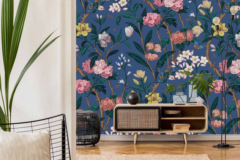 A stylish living room features a dark blue wall with a colorful floral mural. The wallpaper includes vivid reds, soft pinks, lush greens, and touches of gold, creating an eye-catching and vibrant backdrop.