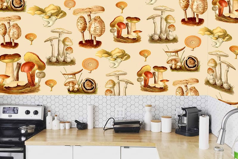 The wallpaper features a colorful and whimsical fungi mushroom pattern. Elements include various types of mushrooms with caps in vibrant hues such as red, orange, blue, green, and yellow. Some mushrooms have polka dots or stripes. The background is a subtle cream color enhancing the playful design without overpowering it. Delicate fern fronds and leaves intermingle with the mushrooms, adding shades of soft greens and browns to the mix.