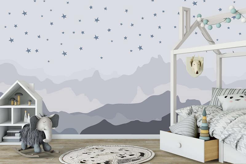 The wallpaper features a mountain and star-themed mural. The mountains are depicted in varying shades of blue and green, with snow-capped peaks. Scattered across the mural are stars in silver and yellow, creating a night sky effect. The background color transitions from a deep navy at the top to lighter blues towards the base, mimicking twilight turning into night.