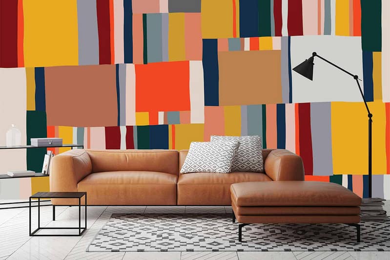 The wallpaper is a colorful, abstract geometric mural featuring bold elements and colors. It includes vibrant hues such as electric blue, fiery red, sunny yellow, deep green, and contrasting black and white shapes. Angular lines and overlapping forms create a dynamic and modern visual impact.