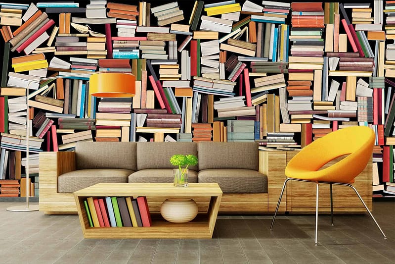 The wallpaper features a vibrant mural of stacked books in various colors, creating a playful illusion of jumbled knowledge on a large bookshelf. Key elements include vibrant, colorful book spines, varying in shades like red, blue, green, yellow, and more. The mural creates an eclectic and lively appearance reminiscent of an overflowing library.
