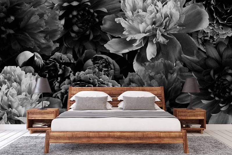 A bedroom wallpaper features an expansive black and white floral mural, dominating the wall behind the bed. The design showcases intricate, oversized blossoms and foliage detailed in stark black lines against a white backdrop. Monochromatic tones emphasize depth and contrast within the floral patterns, creating a dramatic yet elegant focal point in the room.