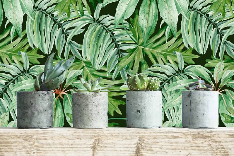 The wallpaper features vibrant green tropical leaves in various shades of green, with hints of lighter greens and deep forest tones. The leaves are lush and detailed, creating a rich, natural look that stands out against any backdrop. This tropical pattern brings the essence of nature indoors with its verdant foliage design.