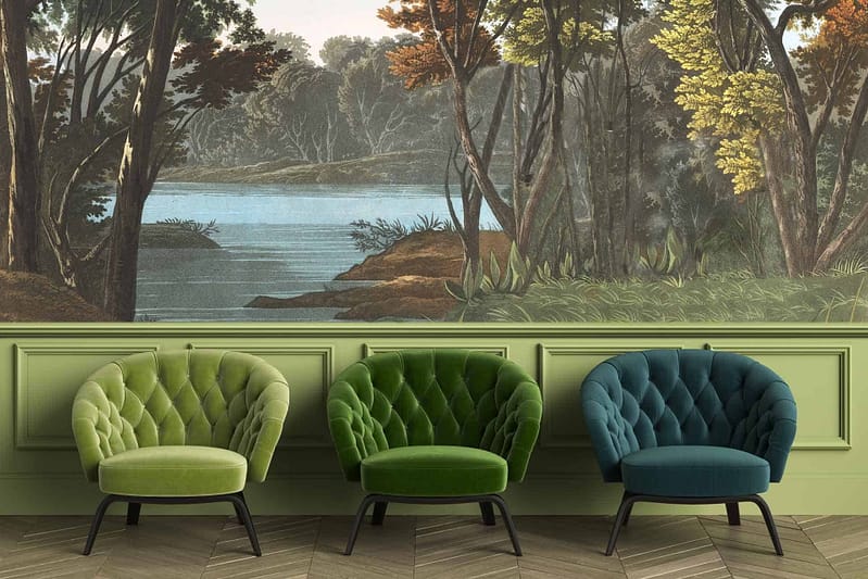 The wallpaper features a serene forest and lake scene, predominantly showcasing shades of green, blue, and brown. Key elements include trees with lush green foliage, a tranquil blue lake, soft earthy tones in the distant landscape, slight reflections of greenery on the water surface, and hints of sunlight filtering through the canopy.