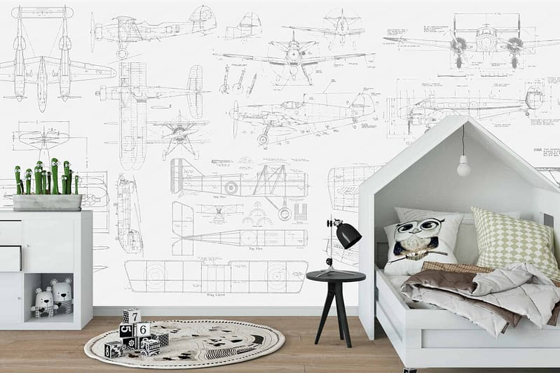 The wallpaper in the child's aviation-themed bedroom features intricate blueprints of vintage airplanes. Highlighted elements include detailed sketches of aircraft components, propeller designs, and fuselage outlines. The color palette primarily consists of soft blues for the blueprint background, contrasted with white and black lines for the technical drawings.