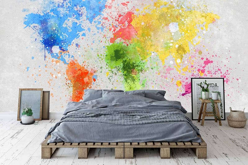 A vibrant, colorful paint splatter mural featuring a mix of bold hues against a white-washed wooden background. The wallpaper incorporates splashes of red, blue, yellow, green, and pink, creating an eye-catching contrast to the serene bedroom decor.