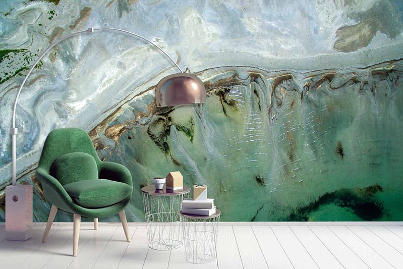 The large wall mural features an abstract, surreal aerial coastal view with swirling turquoise waters, shades of emerald green, sandy beige shores, and hints of coral pink. Elements include fluid wave patterns and subtle transitions between colors evoking a dreamy seascape.