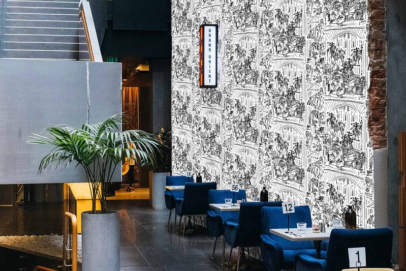 The wallpaper at El Fresco is intricately patterned in black and white. It features ornate designs with high contrast, combining geometric shapes with floral motifs. The detailed patterns make it a striking backdrop in the modern restaurant interior.