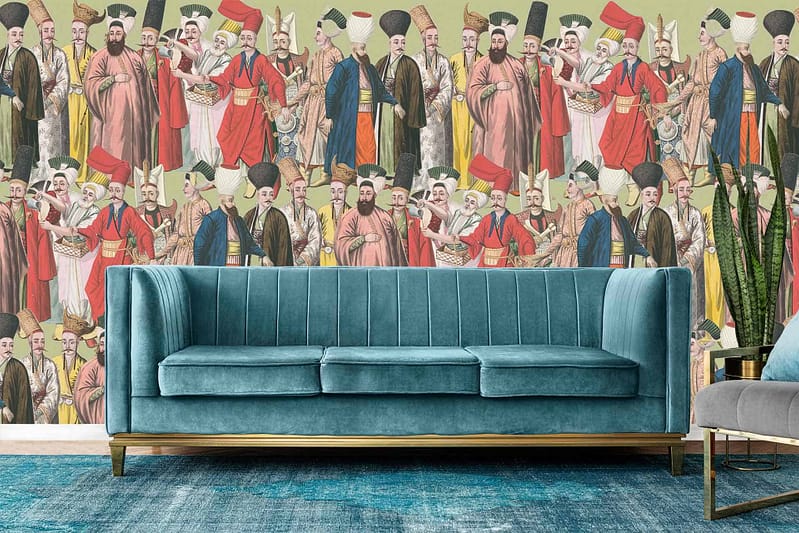 A colorful wall mural depicts an array of historical figures in traditional clothing, featuring vibrant robes and turbans in rich colors such as deep reds, bright golds, lush greens, and royal blues. The scene resembles a grand fashion show with intricate patterns and detailed attire.