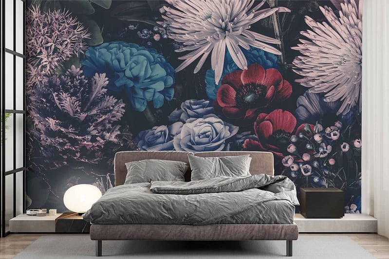 The wallpaper features a large mural of colorful flowers, showcasing vibrant hues such as pink, yellow, blue, and orange. Delicate green leaves and stems add contrast and depth to the design. The floral pattern spreads across the wall behind the bed in a striking yet harmonious arrangement.