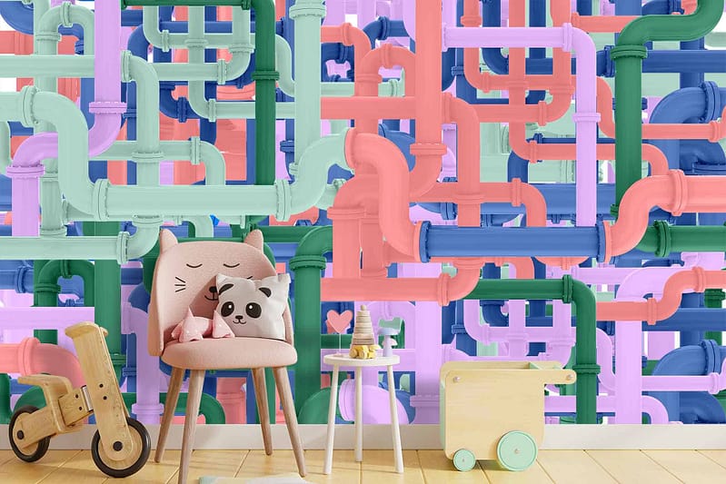 Wallpaper features an array of pastel-colored plumbing pipes in shades of pink, blue, green, and yellow. The playful design is accentuated with whimsical curls and loops. Elements include cat face cushions, panda pillows, drinks and ice cream symbols, wooden toy train motifs on a soft light wood background. Decor is bright and adds a cheerful vibe to the room.
