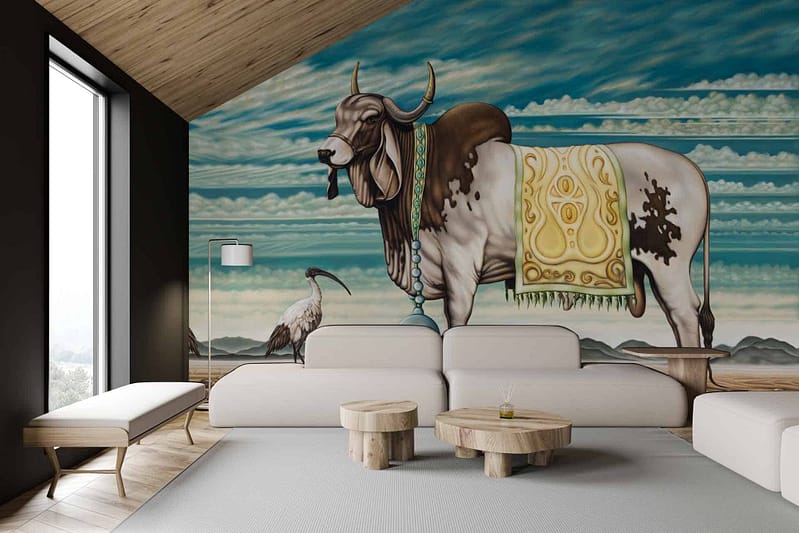 Large wall mural with a decorated cow and bird against a vibrant sky and landscape background. Elements include intricate patterns on the cow, detailed feathers on the bird, and lush greenery. Colors feature bright blue skies, rich green foliage, earthy browns of the landscape, bold reds and golds in the decorations.