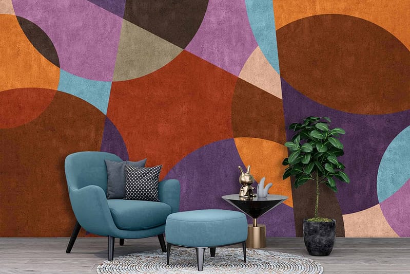 The wallpaper features a vibrant, abstract geometric mural with diverse shapes and colors. Key elements include bold triangles, overlapping circles, sharp zigzags, and fluid wave patterns. Dominant colors are vivid blues, fiery reds, bright yellows, deep greens, and contrasting black accents. The dynamic visuals create an energetic and modern backdrop for the living space.