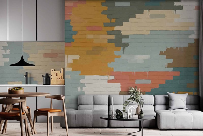 A vibrant abstract mural adorns the brick wall, featuring bold splashes of bright blues, warm oranges, deep reds, and soft yellows. Geometric shapes intermix with fluid patterns, creating a lively yet harmonious atmosphere. The mural’s dynamic composition contrasts beautifully with the room's light gray sectional sofa and enhances the overall modern aesthetic of the space.