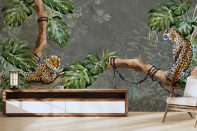 A living room wall mural features two leopards among lush green foliage and tree branches against a muted gray background. The wallpaper combines vibrant greens with neutral tones, showcasing detailed wildlife imagery and natural elements seamlessly.