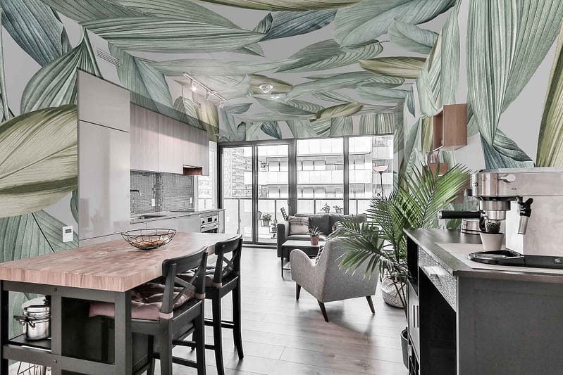 The wallpaper in the modern kitchen and living area showcases large green leaf patterns, creating a nature-inspired design. The dominant elements are oversized leaves with varying shades of green, providing a vibrant and organic ambiance.