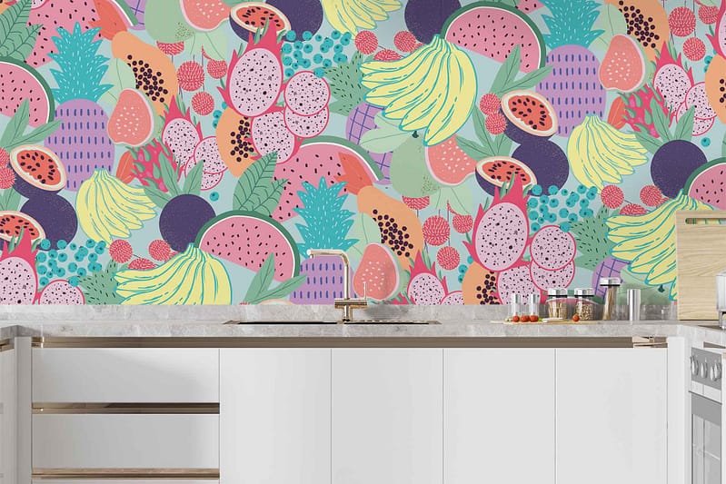 The wallpaper in the modern Carmen-inspired kitchen features vibrant, colorful illustrations of bananas, pineapples, watermelons, dragon fruits, and other tropical fruits. The design is rich with bright yellows, greens, pinks, and reds that create a lively and cheerful atmosphere.
