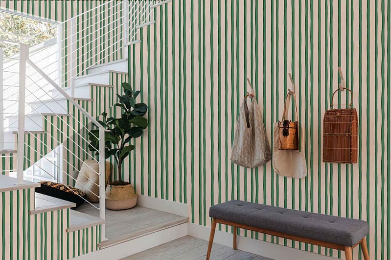 A modern entryway features green-striped wallpaper in mint condition. The stripes vary in shades of green, including mint, sage, and emerald. The design adds a fresh, vibrant touch to the space and harmonizes with natural elements and decor.