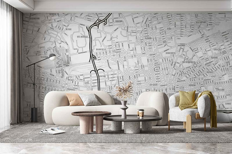 The wallpaper in the modern living room features a large map mural, rich with intricate, maze-like streets and pathways reminiscent of "Streets Have No Name." The color palette primarily consists of monochromatic shades like black, white, and gray, giving it a sleek yet sophisticated look. Key elements include detailed street grids, various line thicknesses to denote road types, and minimalistic geographic markers. The design has a dynamic feel with intersecting lines creating an urban labyrinth effect.