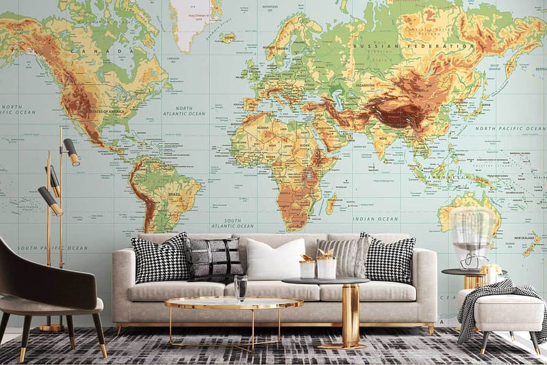 A stylish living room features a large world map mural on the wall. The wallpaper includes elements such as countries, continents, oceans, and borders in neutral shades with subtle highlights. The colors range from earthy tones like beige and taupe to muted blues and greens, creating a sophisticated backdrop.