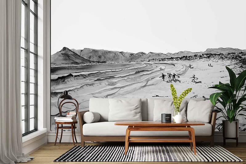 Large black-and-white wallpaper mural depicts a beach scene with distant mountains, waves, and several people running along the sand. Subtle “We Buy Gold” text accents are integrated into the design. Monochrome tones; focus on grayscale imagery with hints of metallic gold in select lettered details.