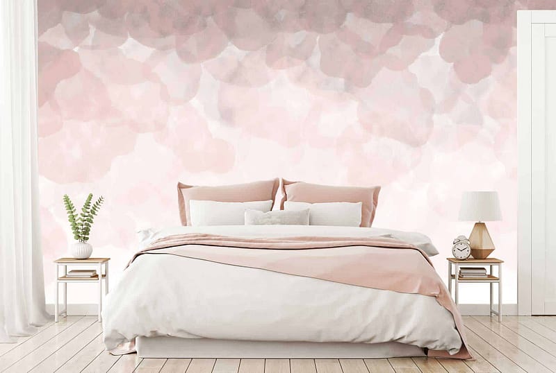 The wallpaper behind the bed features a gradient, abstract design with soft pink and petal hues. The colors blend seamlessly to create a serene ambiance. Hues of blush pink, pastel rose, and delicate whites dominate the pattern, creating a dreamy backdrop for the bedroom. Key elements include smooth transitions between shades and an overall soothing palette.