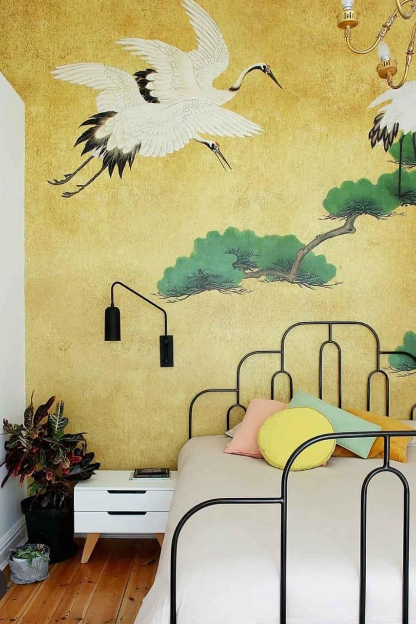 A yellow accent wall features a mural of flying cranes and green trees. The wallpaper elements include cranes in flight and lush green trees set against a vibrant yellow background.