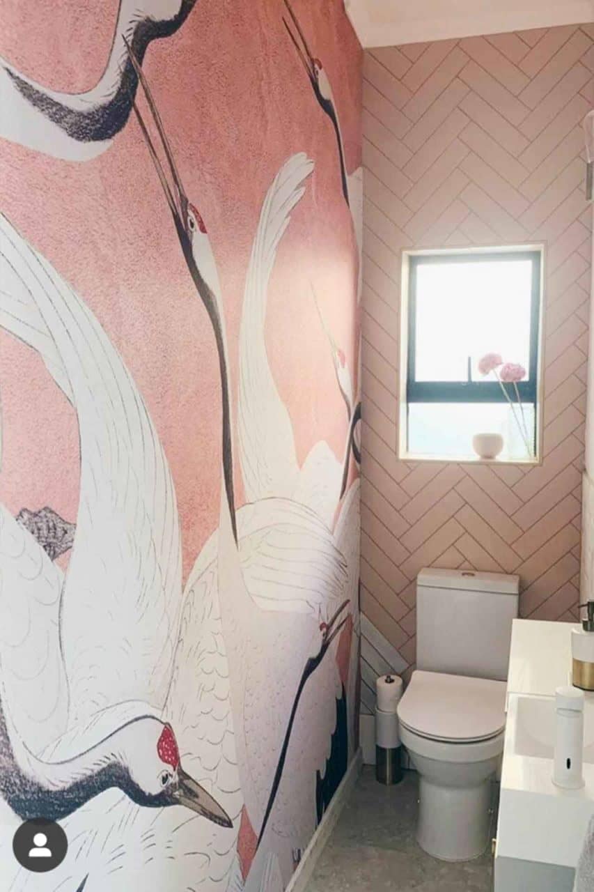 A small bathroom features a standout wallpaper mural of white cranes on a pink background.