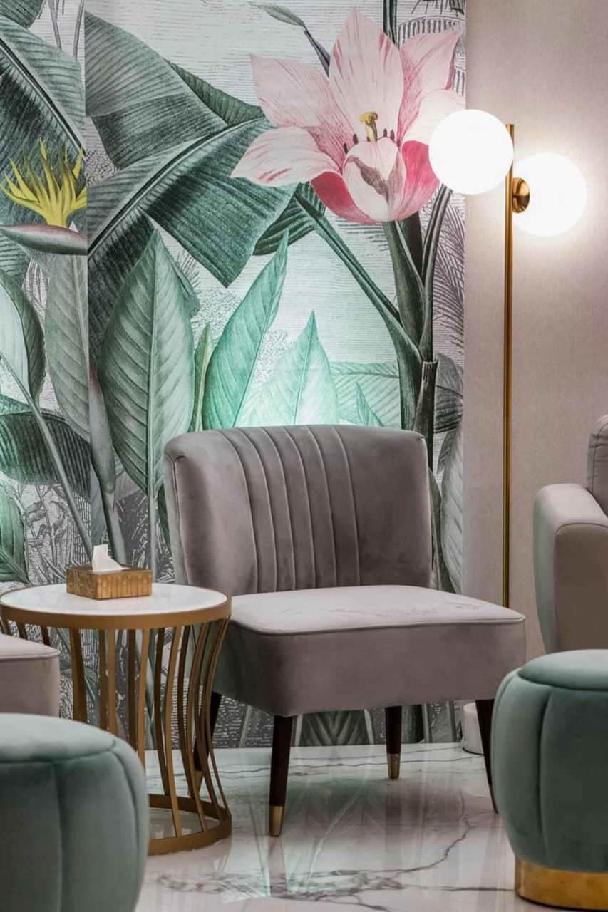 The wallpaper features large green leaves and vibrant pink flowers, creating a tropical floral theme. The foliage offers lush shades of green, while the blossoms range from soft blush to bold fuchsia. Hints of gold may also be present, adding intricate detailing that complements the natural elements. Ideal for drawing attention in an interior design portfolio focused on lively and nature-inspired aesthetics.