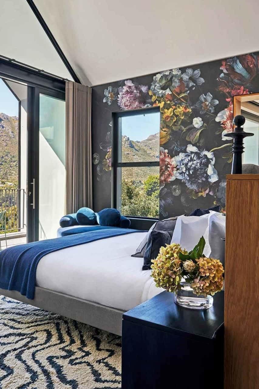 Floral mural wallpaper prominently features delicate blossoms in shades of pink, white, and lilac with green leaves. The intricate design blends traditional and contemporary elements, creating a sophisticated backdrop for the bedroom.