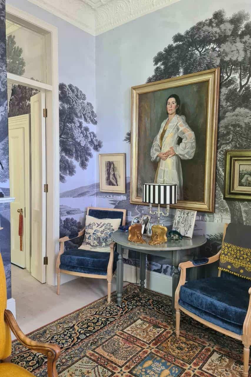 The wallpaper in the cozy corner features an artistic depiction of intertwined trees, evoking an artist's portfolio. The background blends soft, muted tones of cream and beige, while the tree illustrations are rendered in delicate shades of green, brown, and gold. The intricate patterns and subtle contrasts make it a focal point in the room’s design.