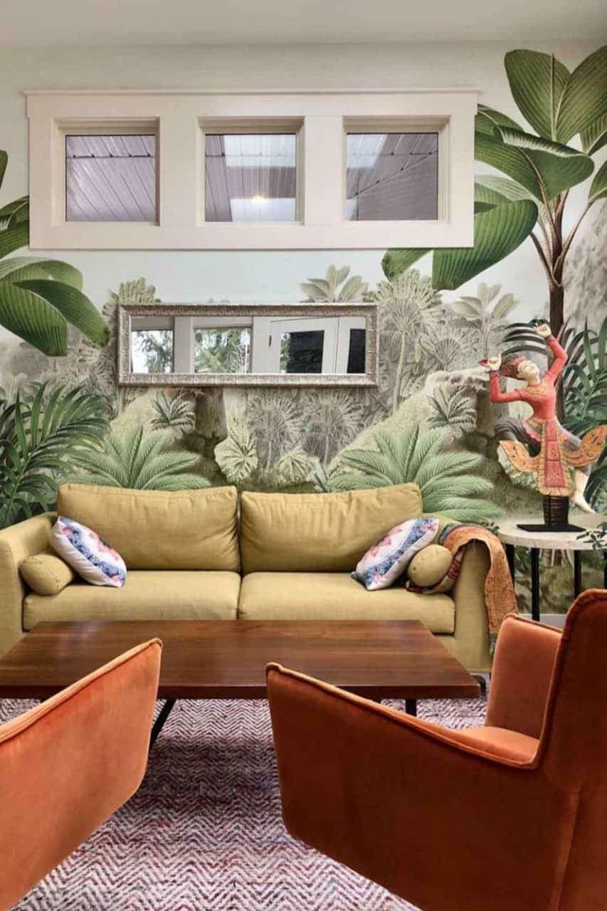 The living room's walls are adorned with a lush, tropical-themed mural. This wallpaper features vibrant greens, deep blues, and rich earth tones, portraying large tropical leaves and exotic flora. Hints of bright florals in reds and yellows pop against the verdant background, creating an immersive jungle feel that adds depth and nature-inspired charm to the space.