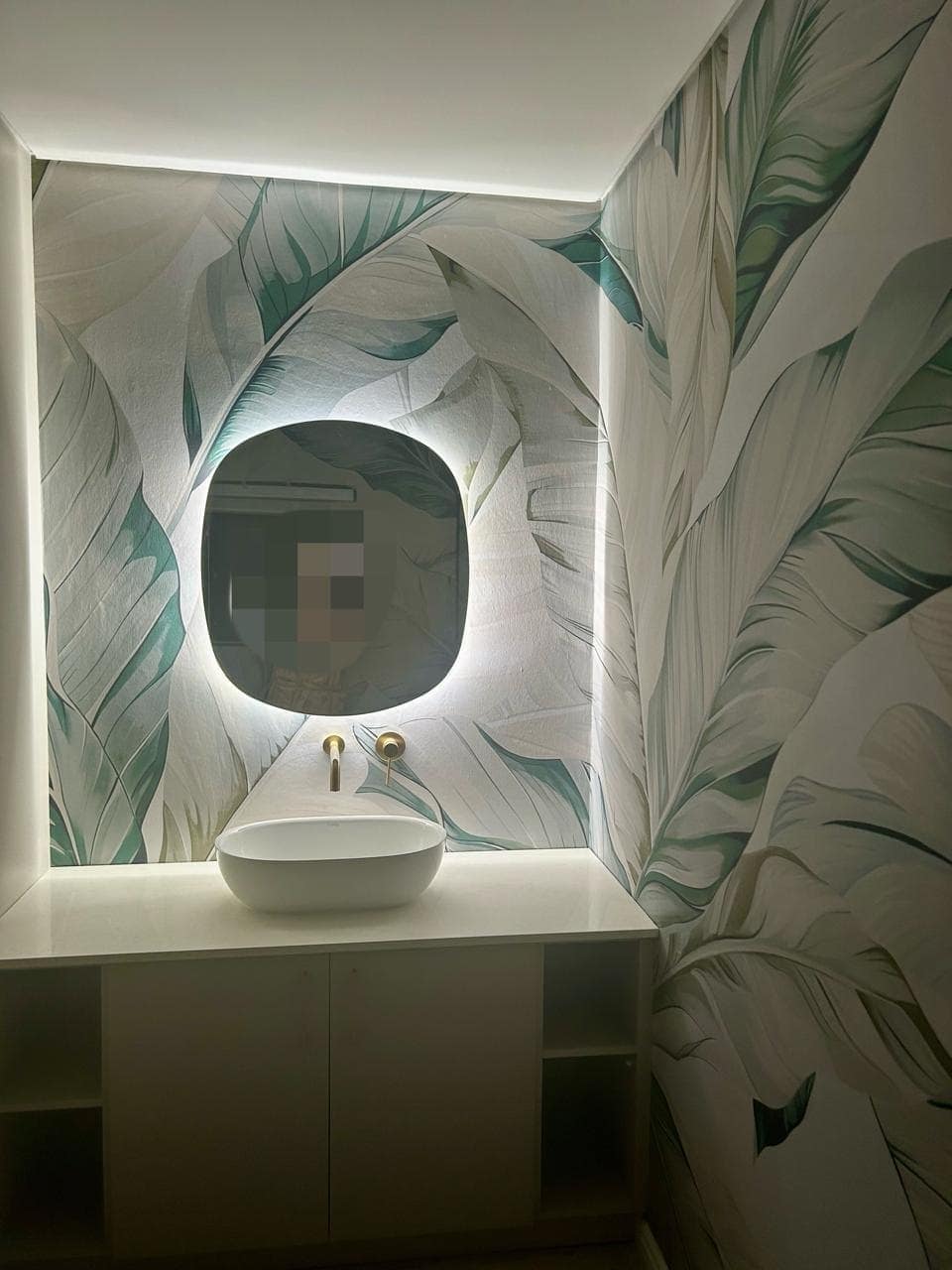 Discover a modern bathroom adorned with striking tropical leaf-patterned wallpaper. The design features lush green leaves, vibrant emerald hues, subtle gold accents, and hints of deep teal. Perfect for creating a stunning focal point, this wallpaper adds an elegant yet exotic touch to any contemporary space. Ideal for your chic and stylish portfolio.
