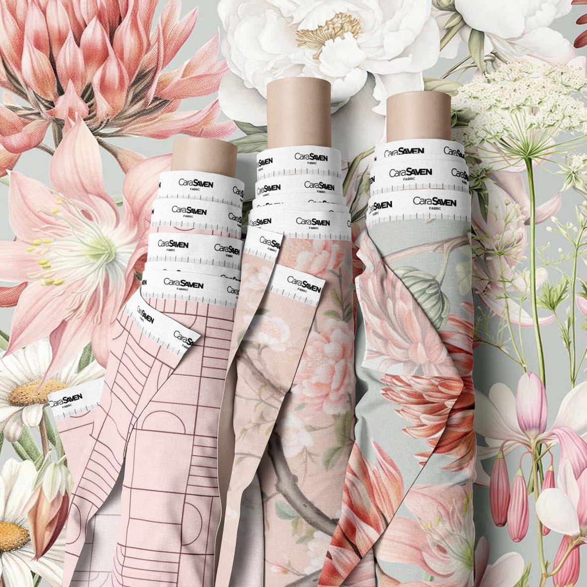 Large-scale floral wallpaper featuring prominent flower illustrations in shades of pink, cream, and green. The design has a soft, elegant palette with botanically inspired details and watercolor-style blooms reminiscent of designer wallpapers by Cara Saven.