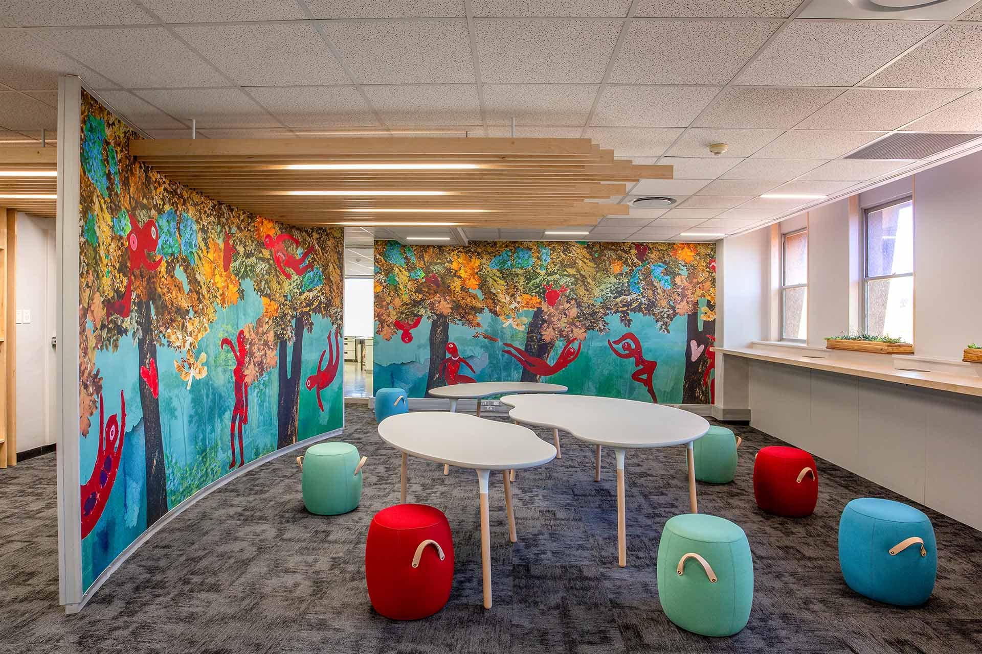 Brightly lit room wallpaper features whimsical forest scenes with vibrant animals. It showcases colorful elements such as lush green trees, playful woodland creatures, and lively flowers in various hues. The mural bursts with shades of blue, yellow, red, and green, creating an enchanting backdrop.