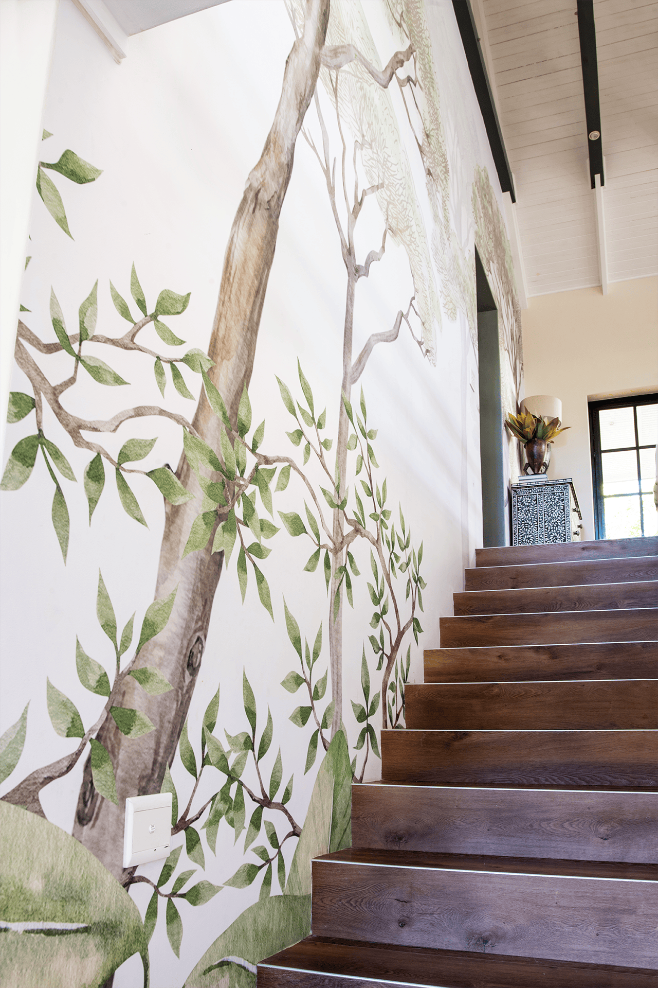 The wallpaper features a large mural of a tree with detailed branches and green leaves, creating a natural and serene atmosphere. The colors prominent in the wallpaper are shades of green (for the leaves) and shades of brown (for the tree branches).