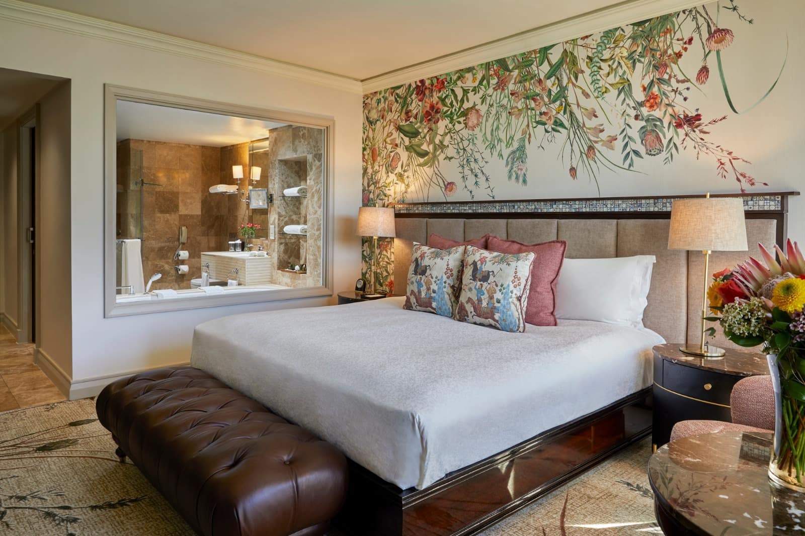 Floral accent wall featuring bold, colorful flower patterns in pink and green hues stands out behind the bed. The wallpaper showcases large blossoms and leafy motifs, adding a vibrant botanical touch to the hotel room.