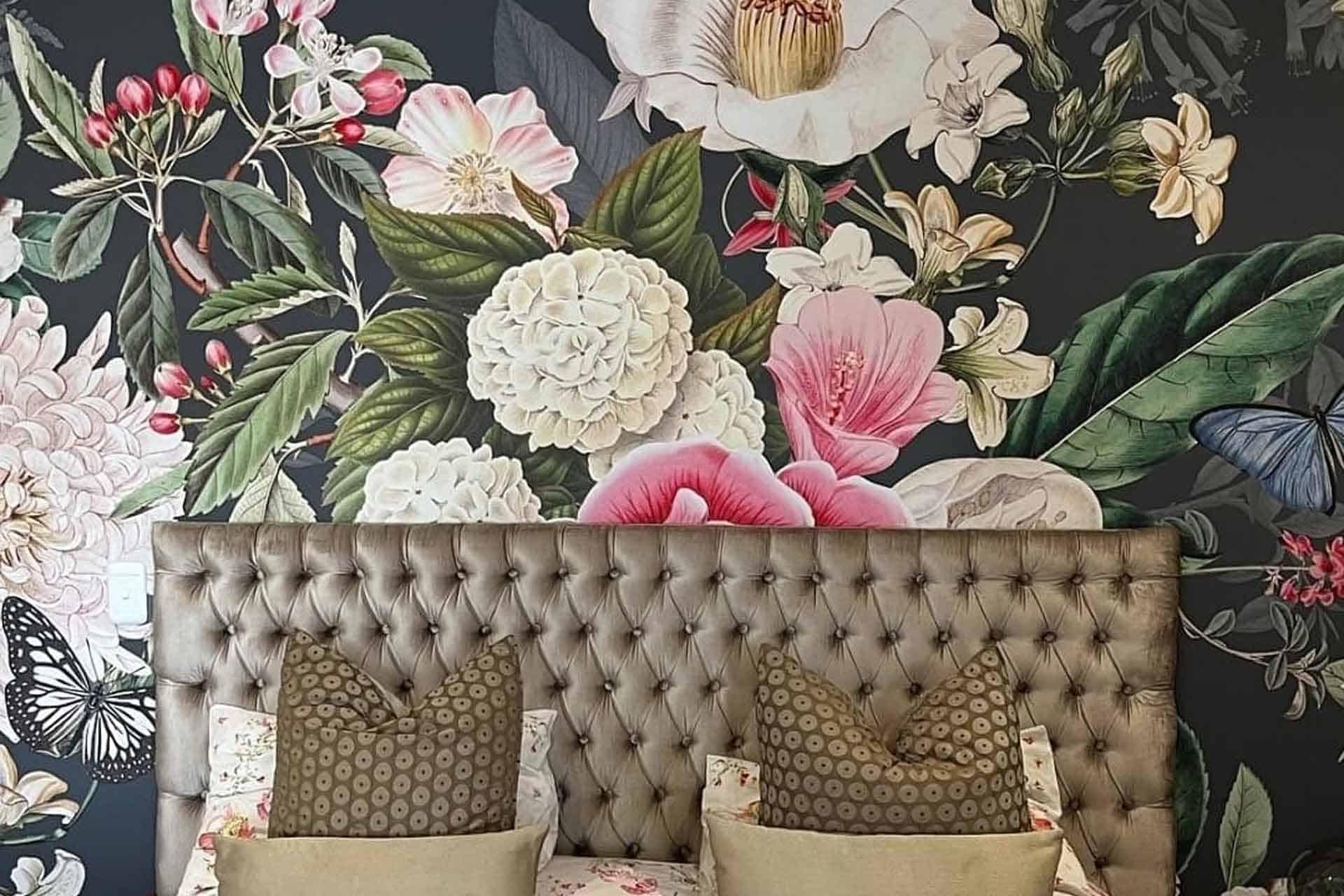 The wallpaper features a vibrant floral pattern with large flowers, leaves, and butterflies. The design includes detailed images in dynamic colors such as bold reds, soft pinks, lush greens, bright yellows, and deep blues. This colorful background transforms the bedroom into an elegant retreat by providing lively visual interest through its intricate botanical elements.