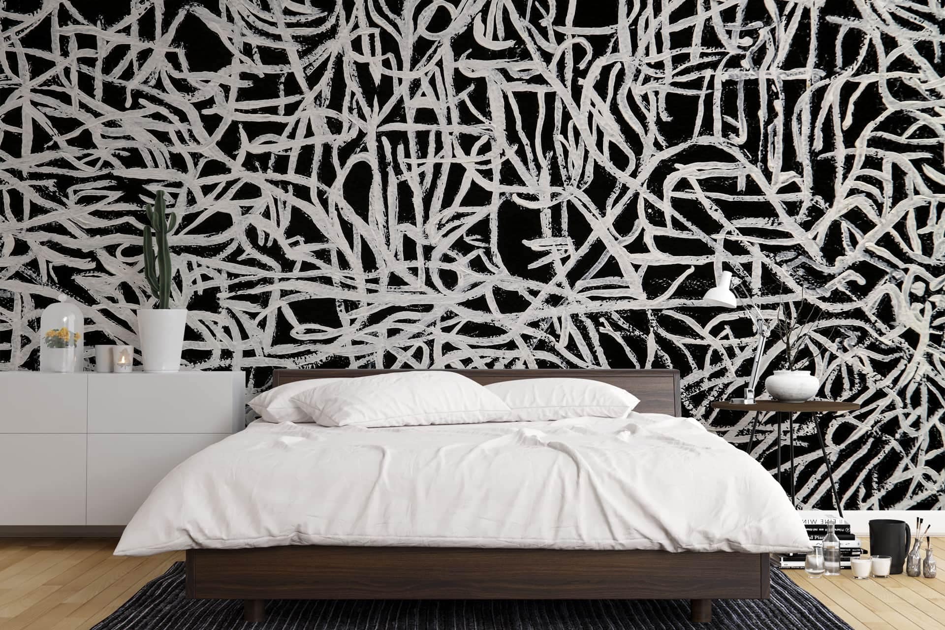 The wallpaper behind the bed is an abstract black and white mural. It features intricate patterns, bold lines, and striking contrasts between black and white elements. The design includes swirling shapes, geometric figures, and possibly some splashes or brush strokes in varying intensities of black against a white background.