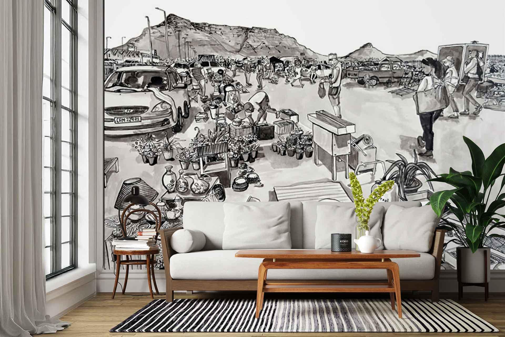 Black and white wall mural featuring a detailed busy outdoor market scene; includes people, cars, street vendors, tents, and distant mountains. The artwork is monochromatic with high-contrast black ink linework and shading on a white background.