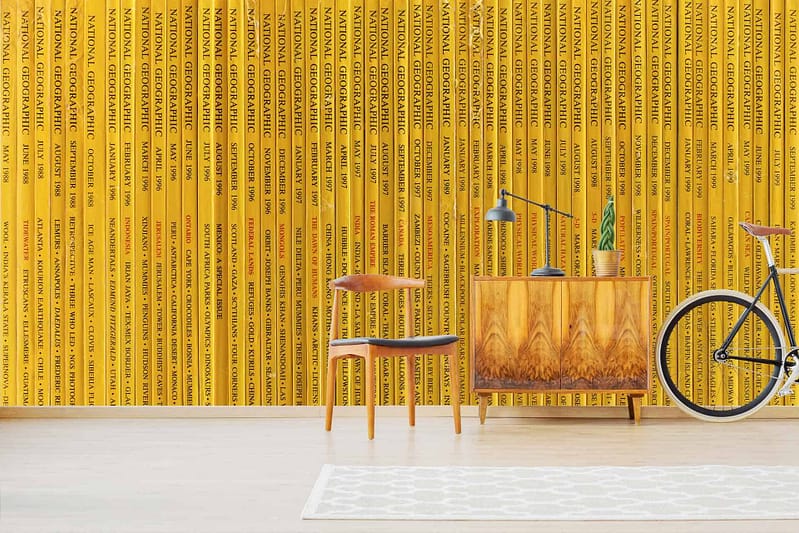 The wallpaper showcases vertically arranged yellow National Geographic magazine spines, creating a vibrant and adventurous ambiance. The prominent color is the bright, bold yellow of the magazine spines. The vertical arrangement emphasizes a sense of order and curiosity, with small text details adding subtle complexity to the overall design.