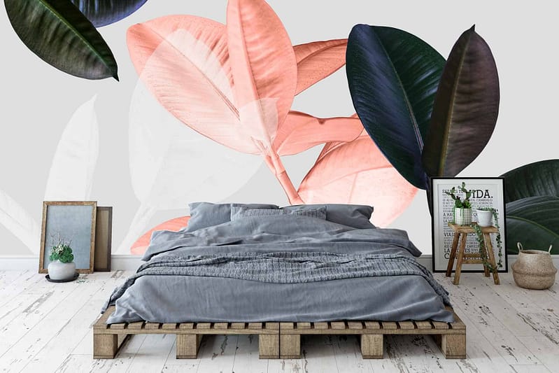 A bedroom with a wooden pallet bed frame features a wall mural displaying large, colorful leaves. The wallpaper showcases shades of pink, green, and black, creating an eye-catching botanical design.
