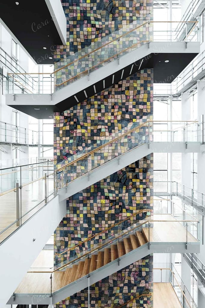 The wallpaper features a colorful, mosaic-like pattern made of small, rectangular tiles. Elements include vibrant hues such as deep blues, rich reds, lush greens, and bright yellows. The artistic design adds a dynamic and contemporary touch to the sleek interior.